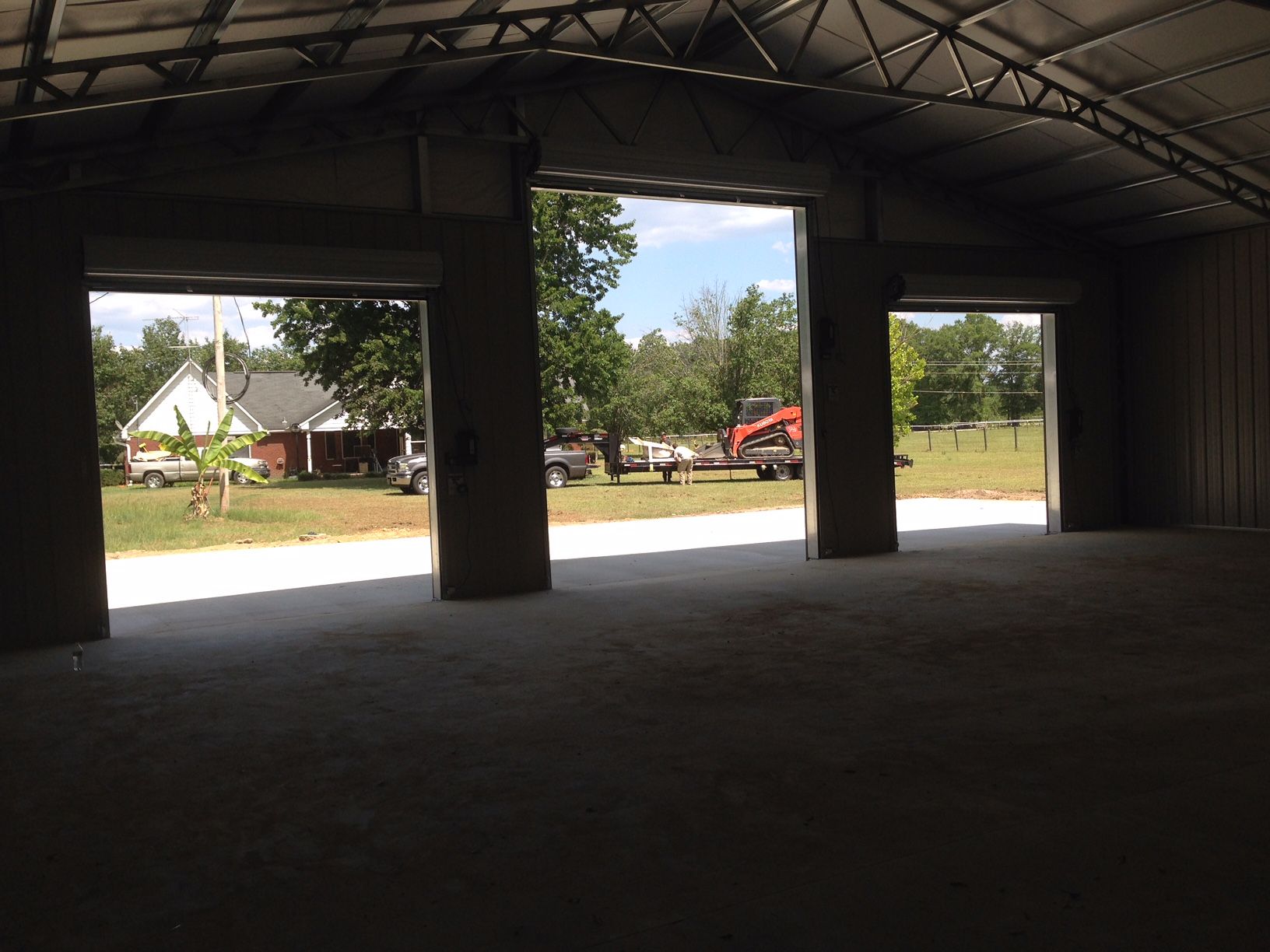 An empty garage with the doors open and a tractor in the background