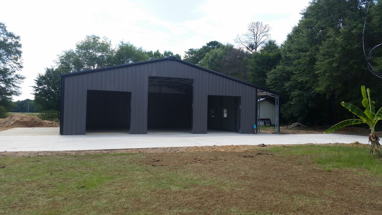 A large metal building with three garage doors is sitting on top of a lush green field.