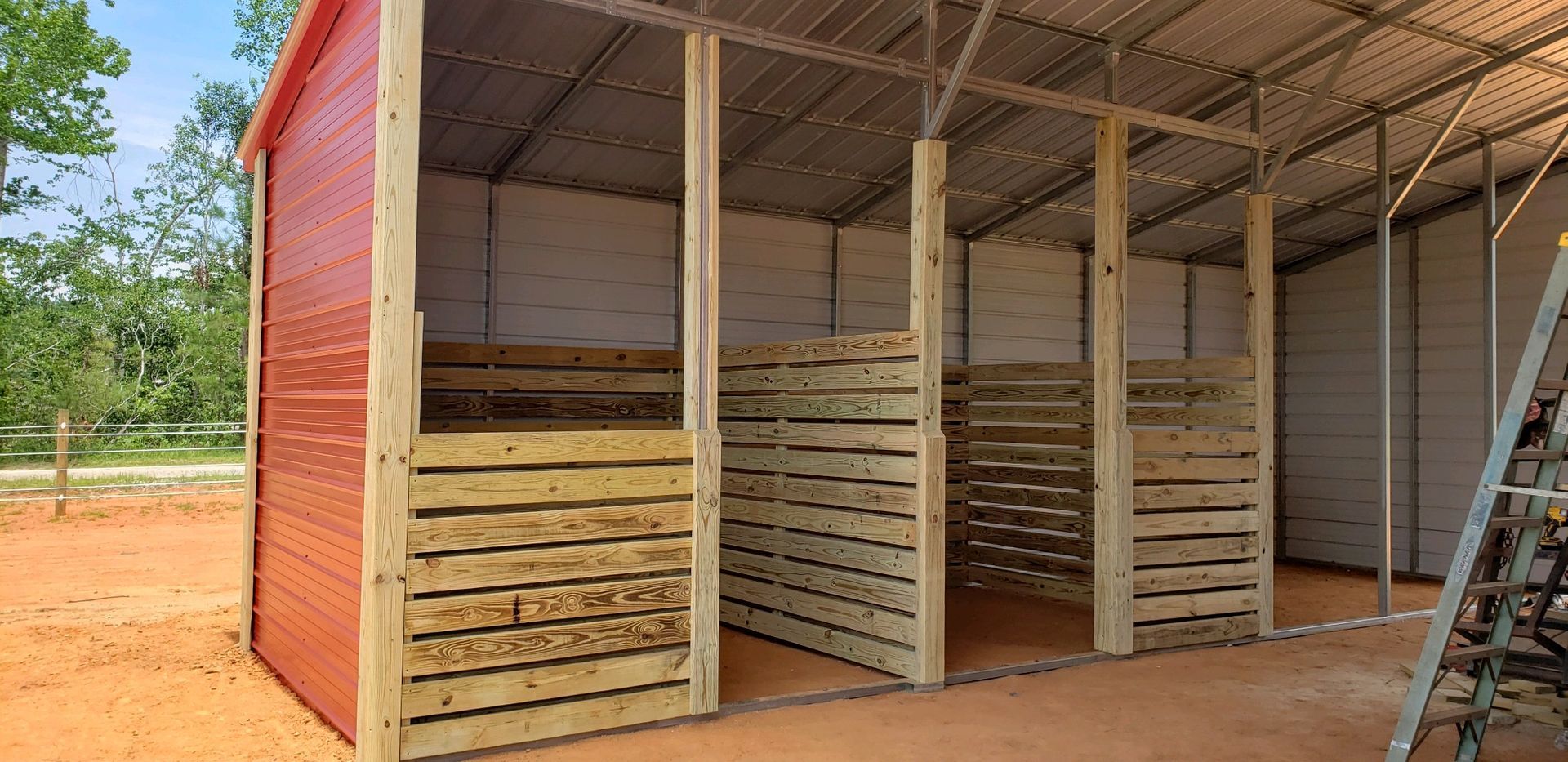 A red barn with wooden walls is being built on a dirt field.