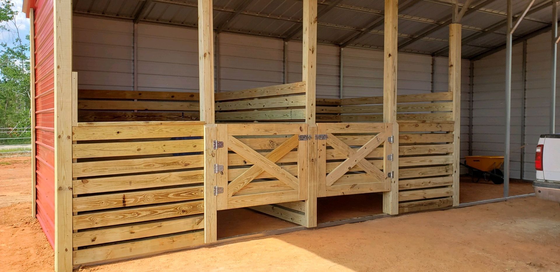 A horse stable with wooden fences and a red barn in the background.