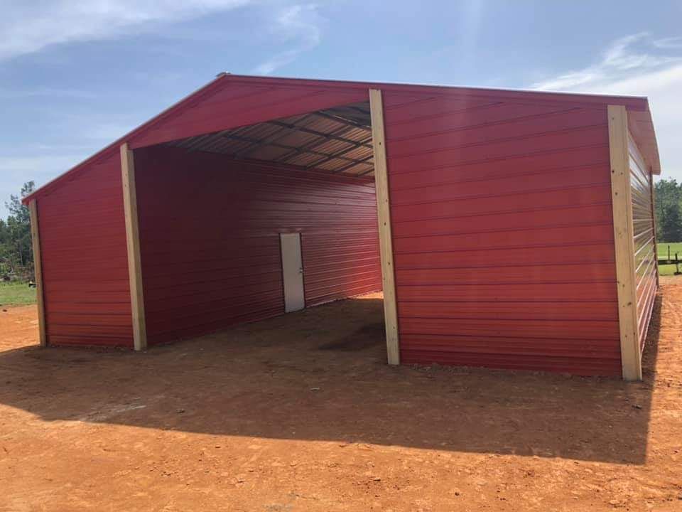 A large red barn is sitting on top of a dirt field.