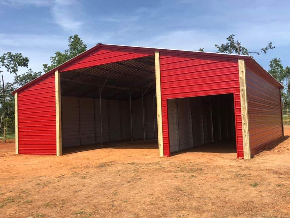 A large red barn is sitting in the middle of a dirt field.