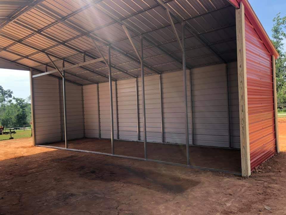 A large metal building with a red roof is sitting on top of a dirt field.