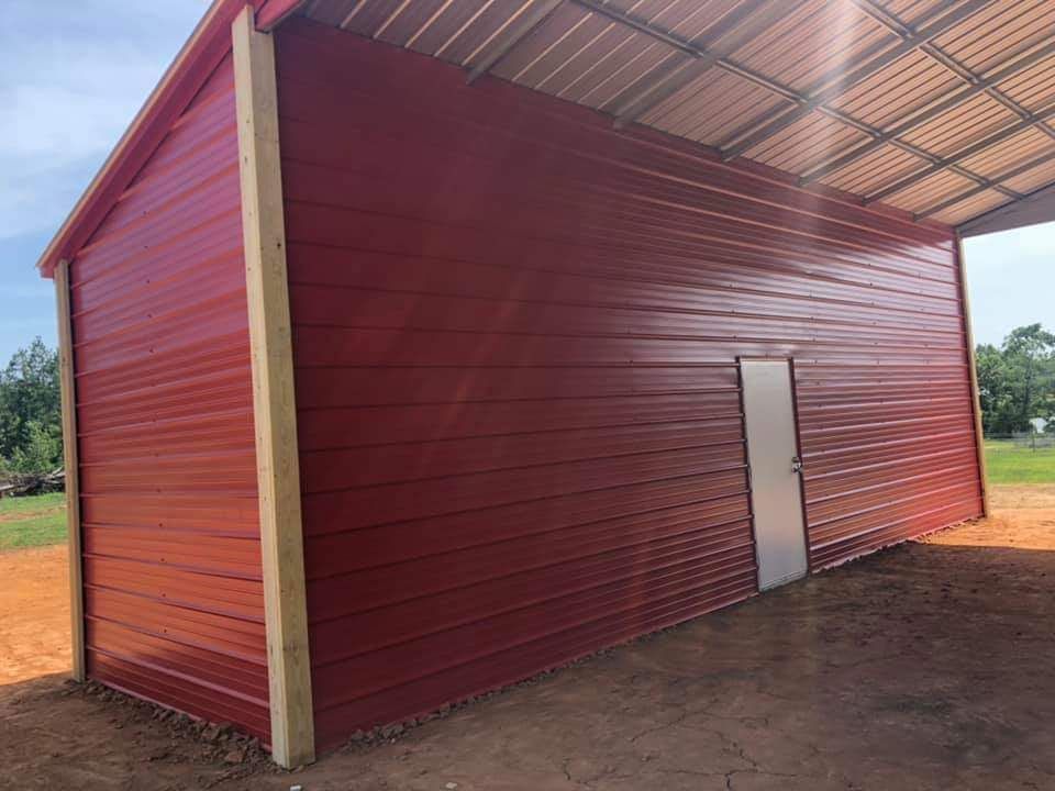 A red metal building with a white door is sitting on top of a dirt field.