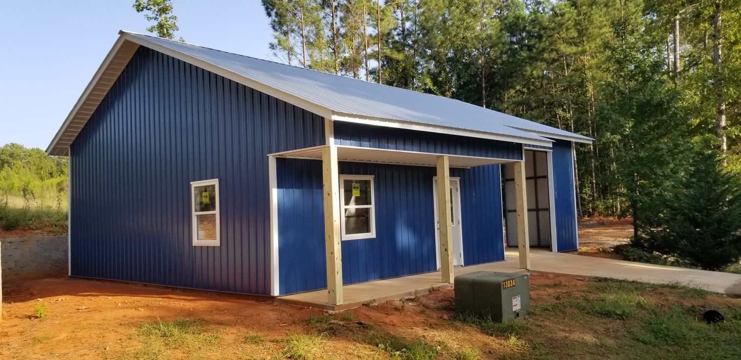 A blue metal building with a porch and windows is sitting on top of a dirt field.