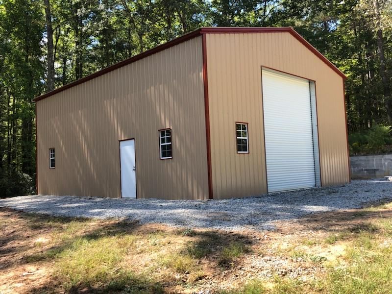 A large metal building with a white garage door is sitting in the middle of a field.