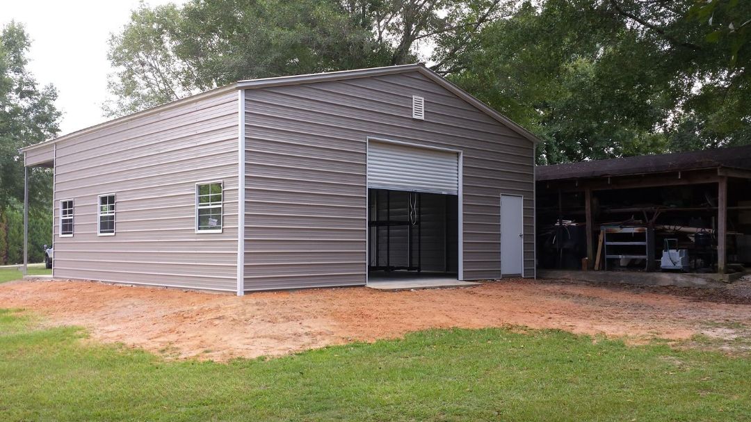 A large metal building with a garage door is sitting in the middle of a grassy field.