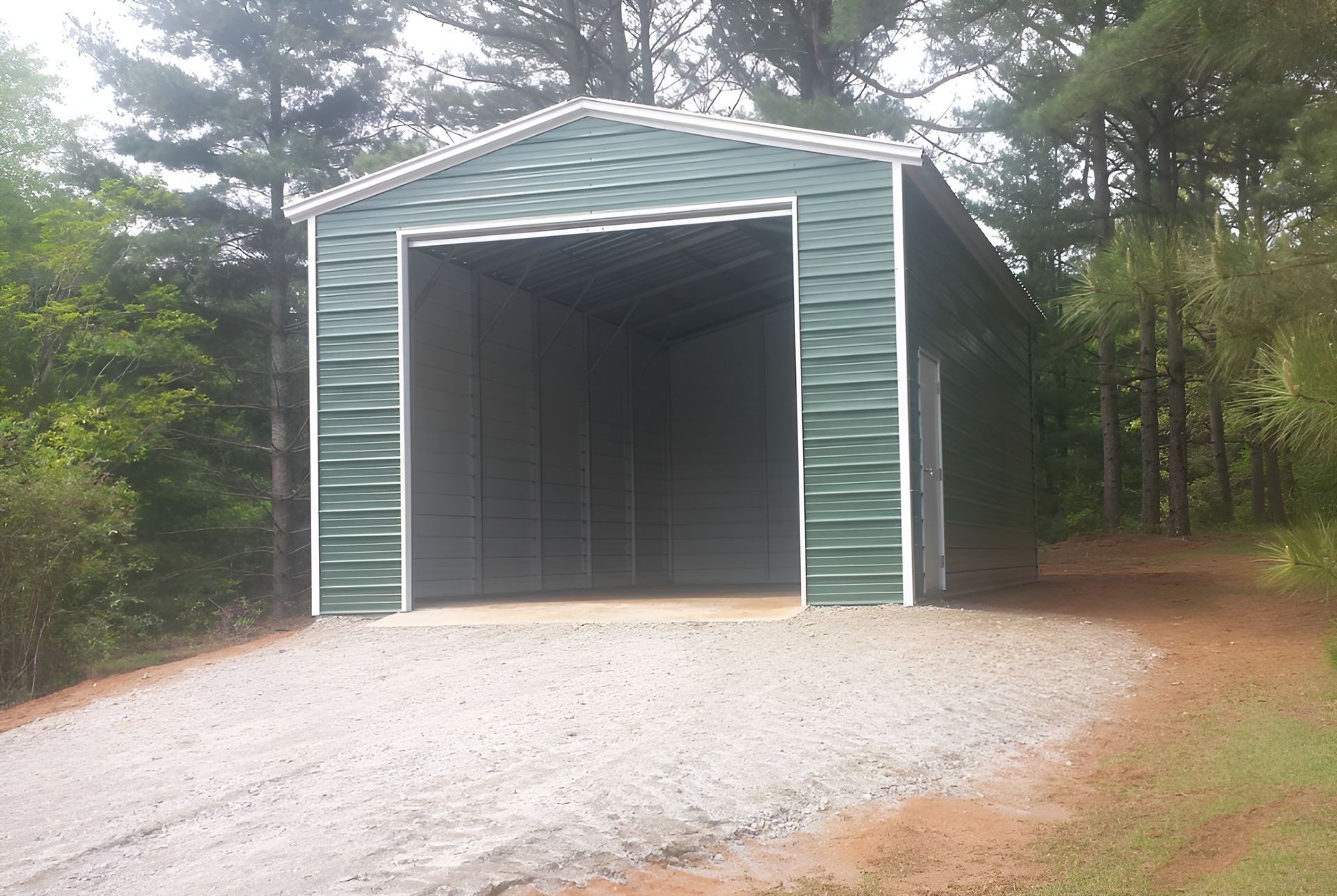 A green metal garage is sitting on the side of a gravel road.