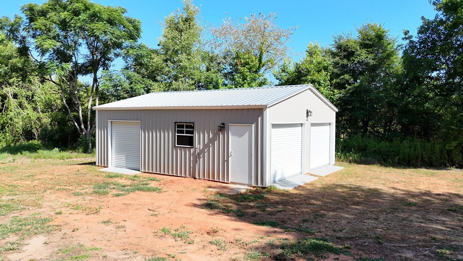 A garage with two garage doors is sitting in the middle of a dirt field.