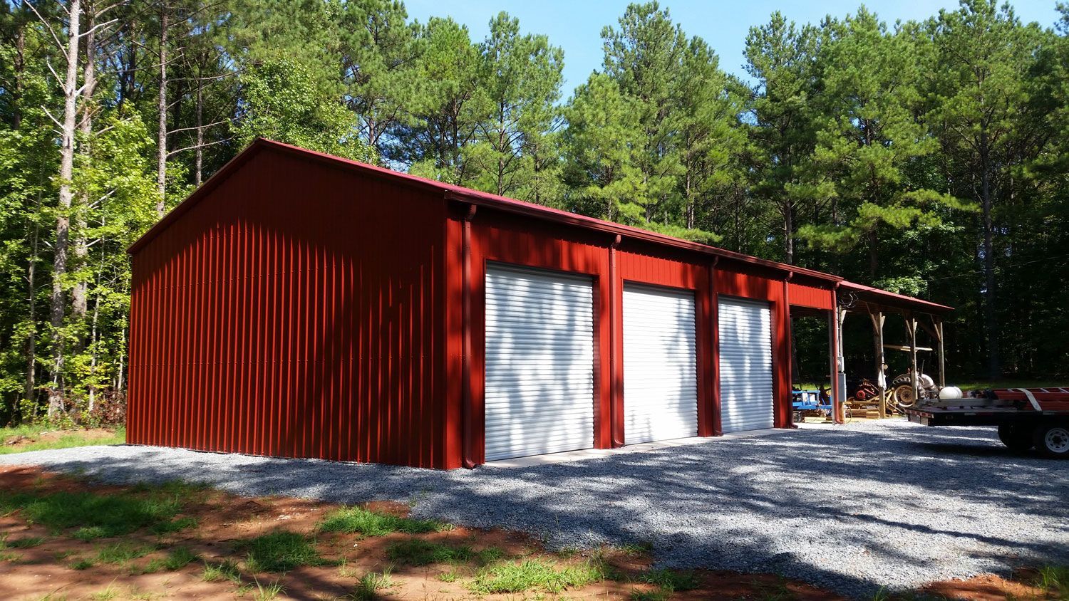 A red barn with white doors is in the middle of a forest.