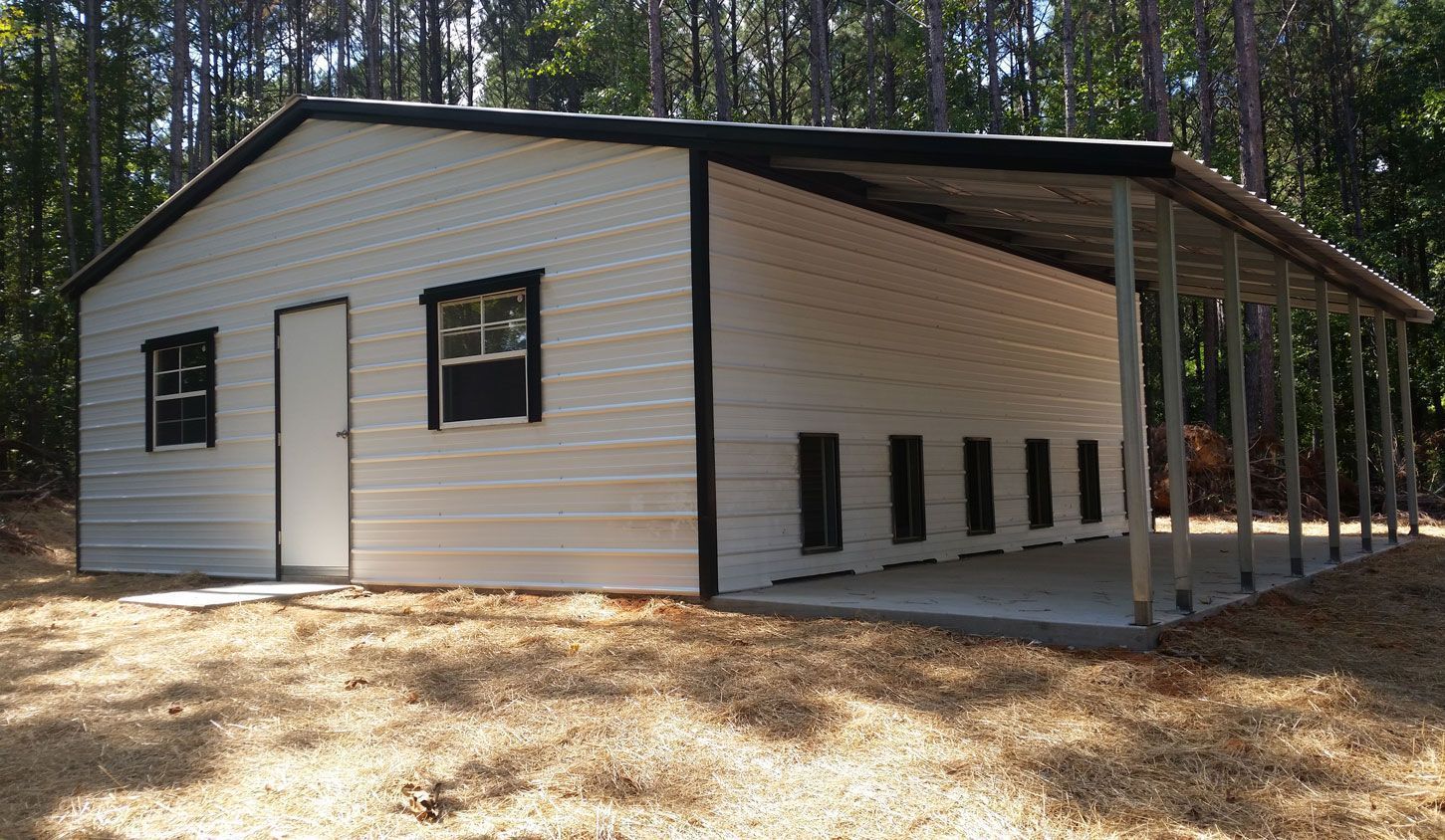A white metal building with a black roof is sitting in the middle of a field.