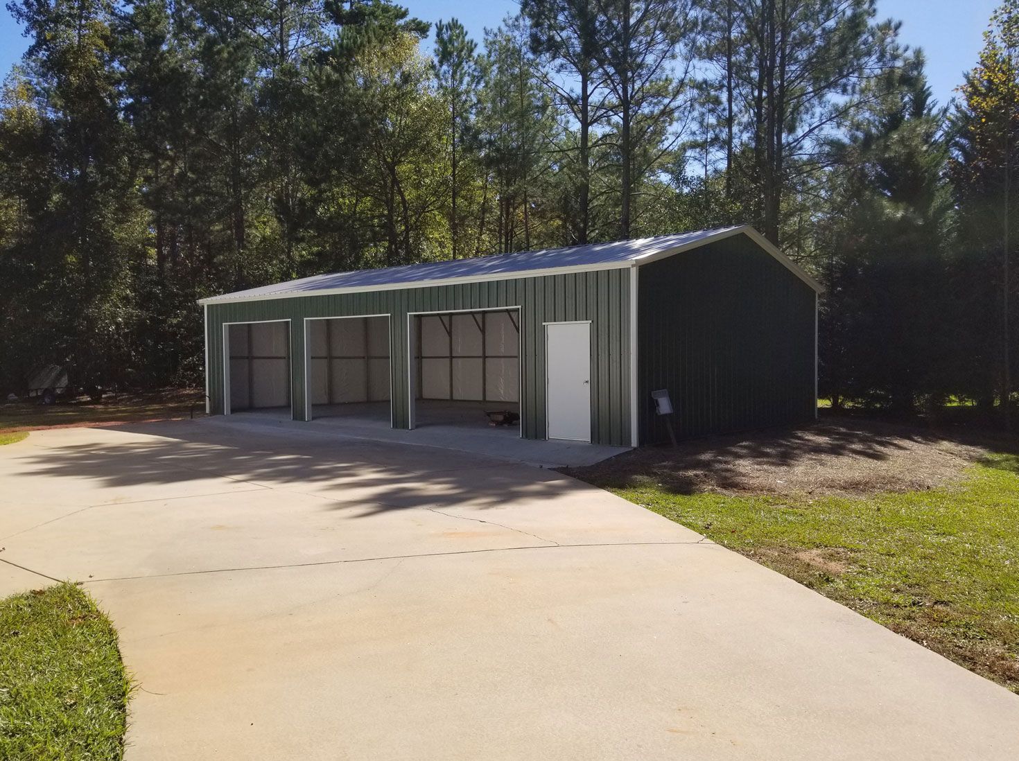 A green metal garage with a driveway in front of it.