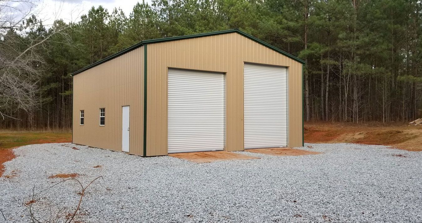 A metal garage with two garage doors is sitting on top of a gravel lot.
