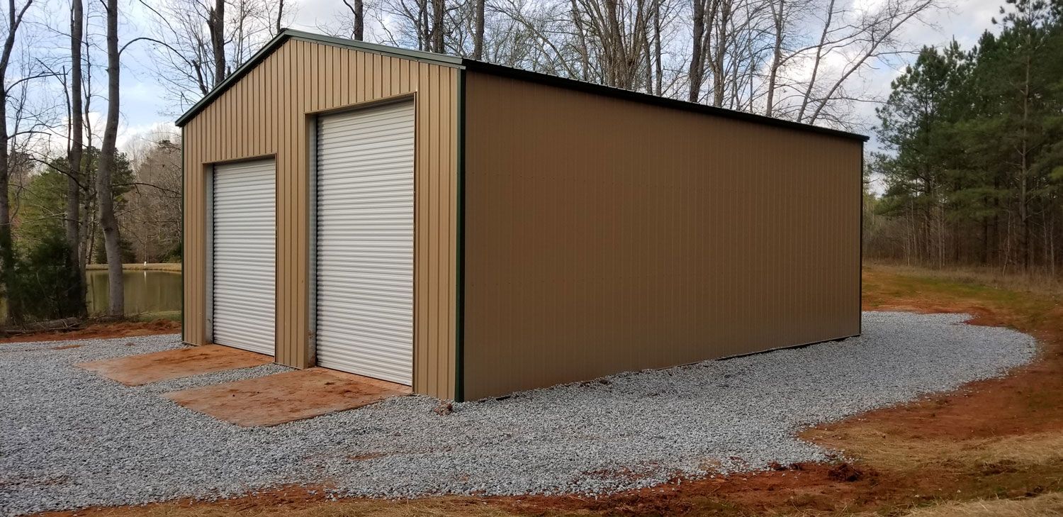 A metal shed with two garage doors is sitting in the middle of a gravel driveway.