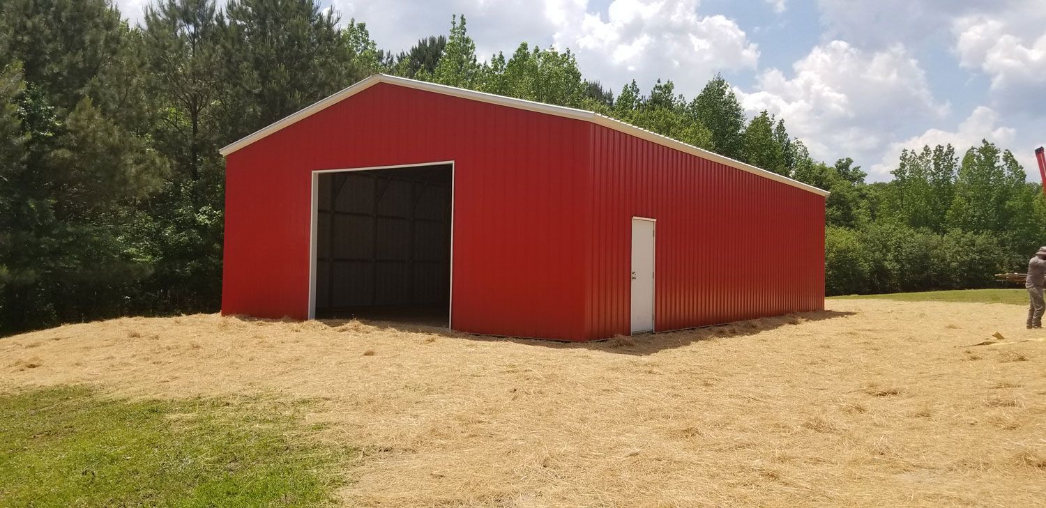A large red barn is sitting in the middle of a dirt field.