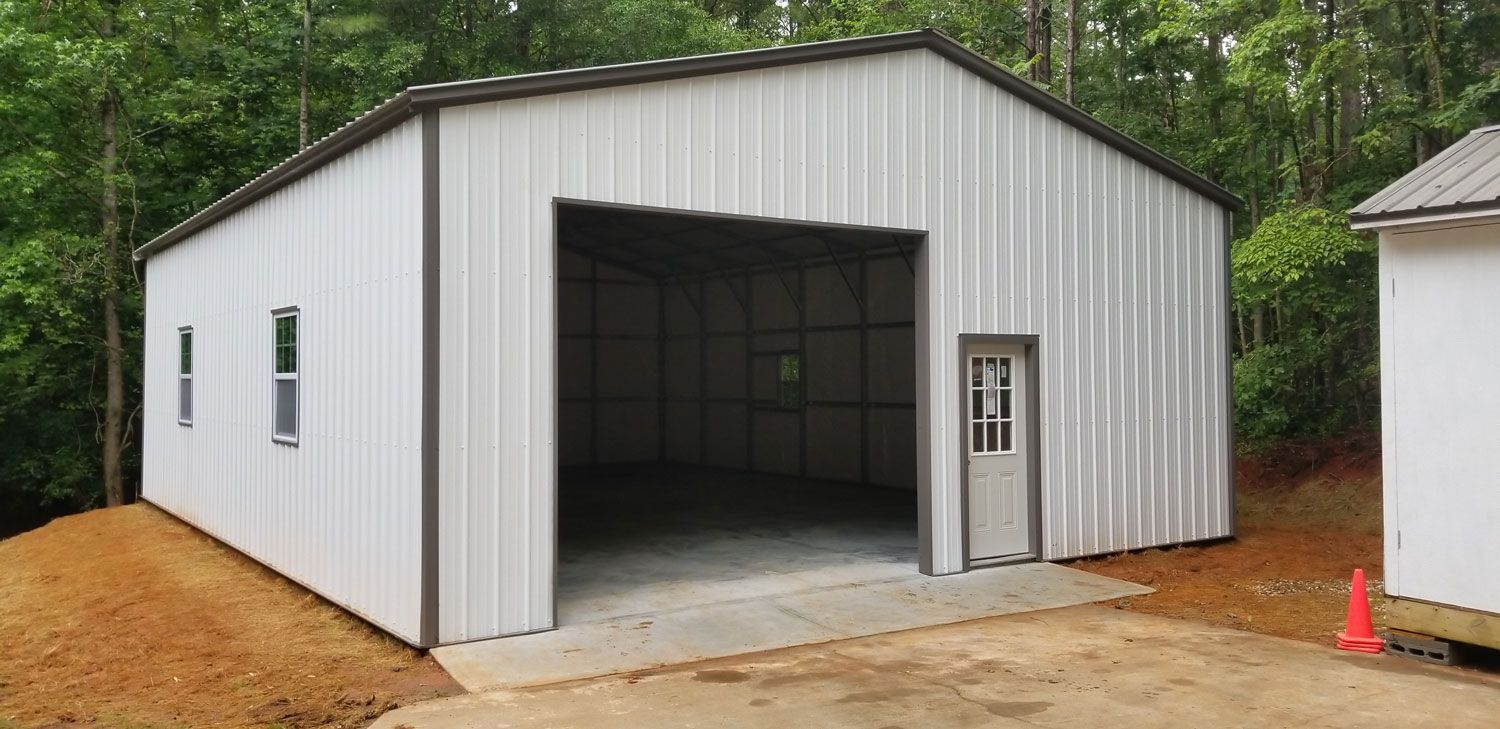 A white metal garage with a large door is sitting on top of a dirt hill.
