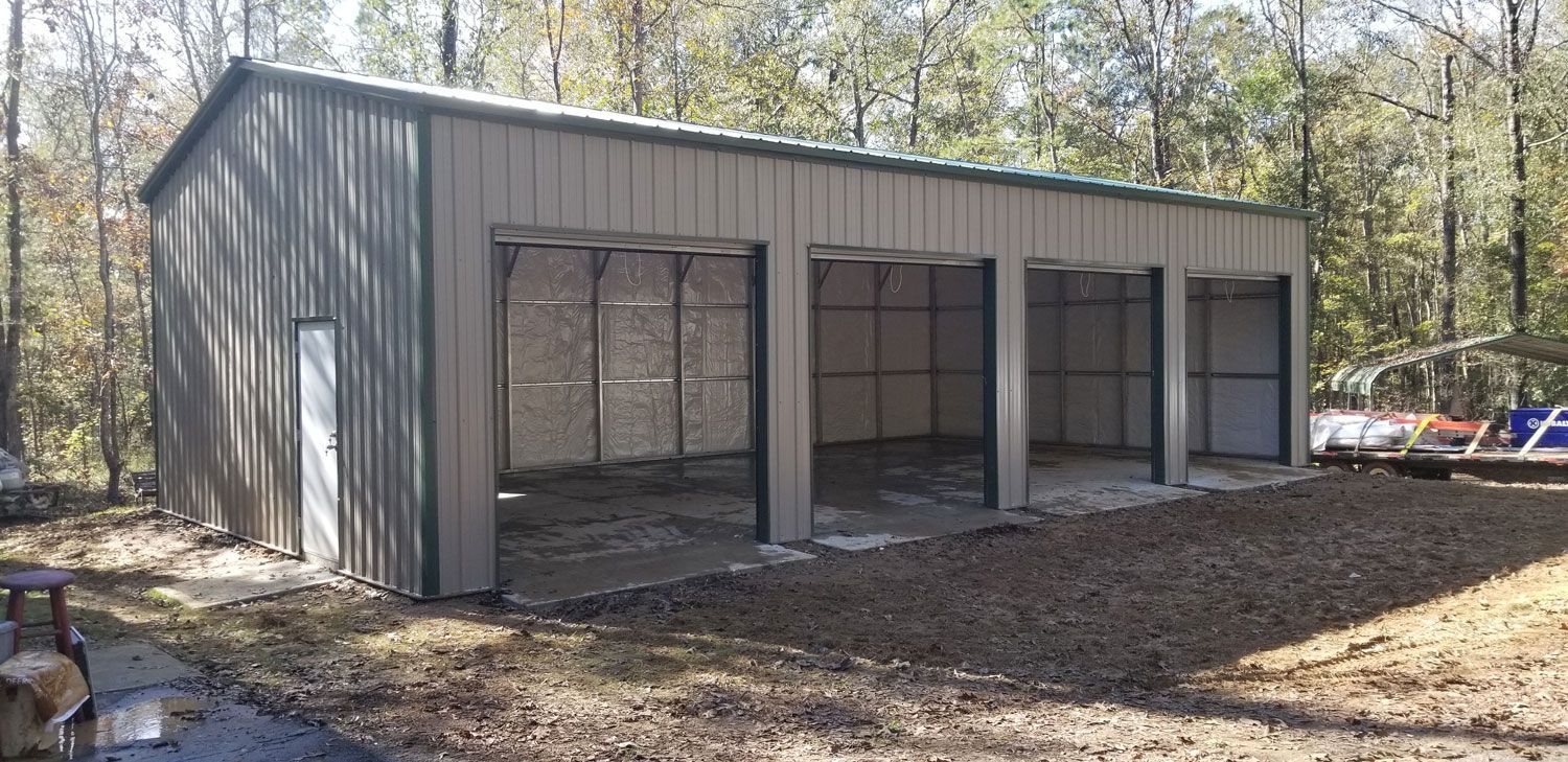 A large metal garage is sitting in the middle of a dirt field.