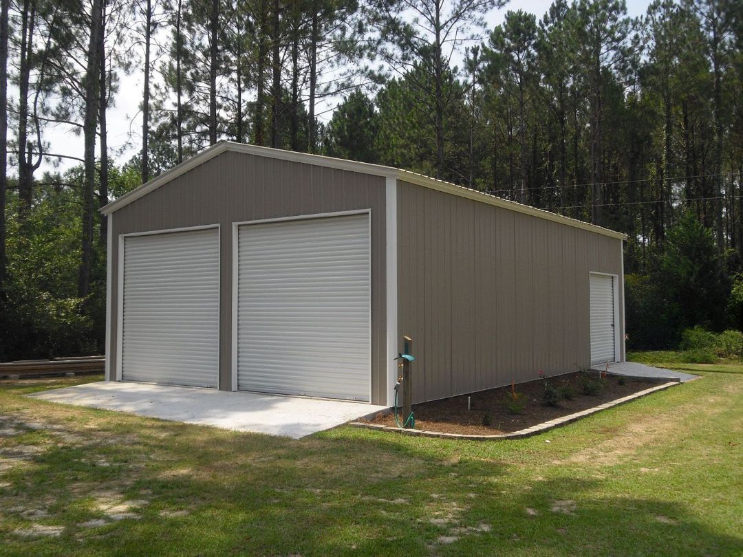 A garage with two garage doors is sitting in the middle of a lush green field.