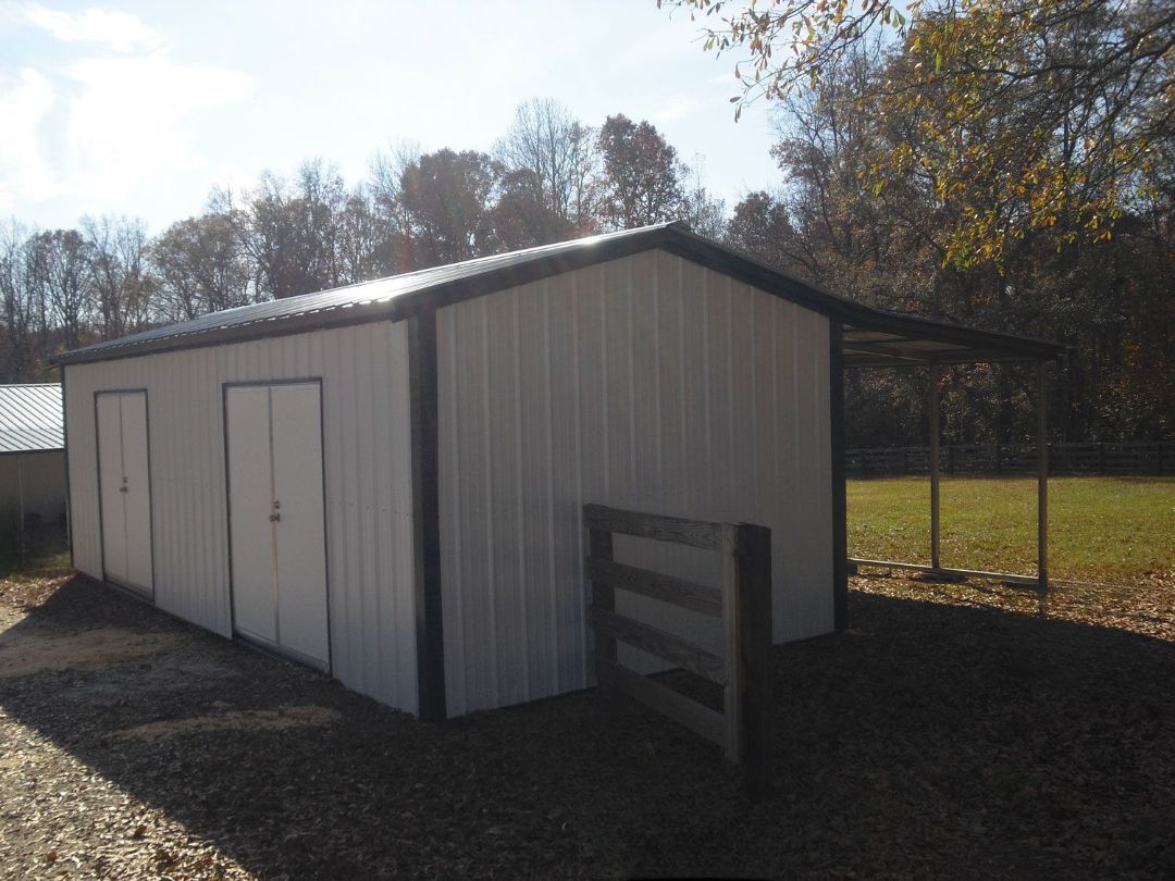 A white shed with black trim sits in the middle of a field