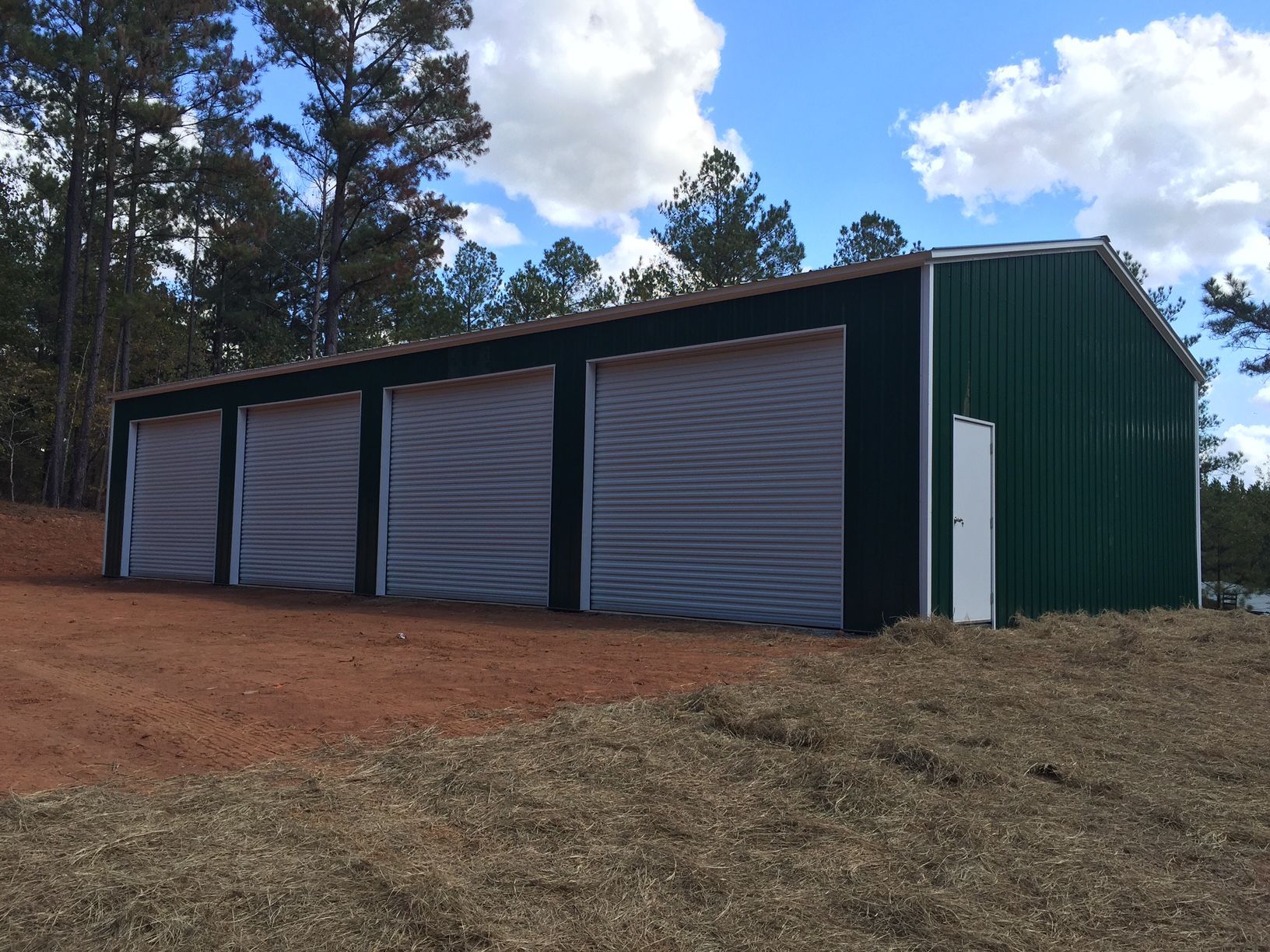 A green garage with white doors is sitting in the middle of a dirt field.