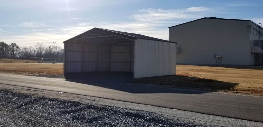 A small white building is sitting on the side of a road next to a building.