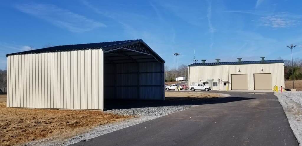 A metal building with a black roof is sitting next to a large building.