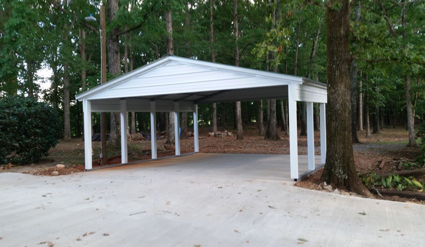 A white carport is sitting in the middle of a driveway surrounded by trees.