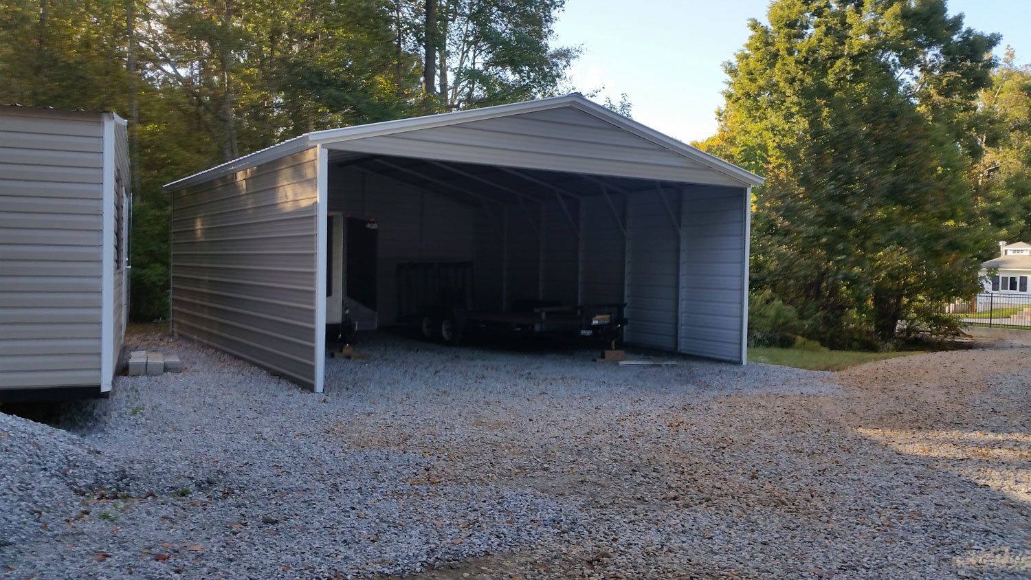 A metal garage with a trailer parked underneath it.