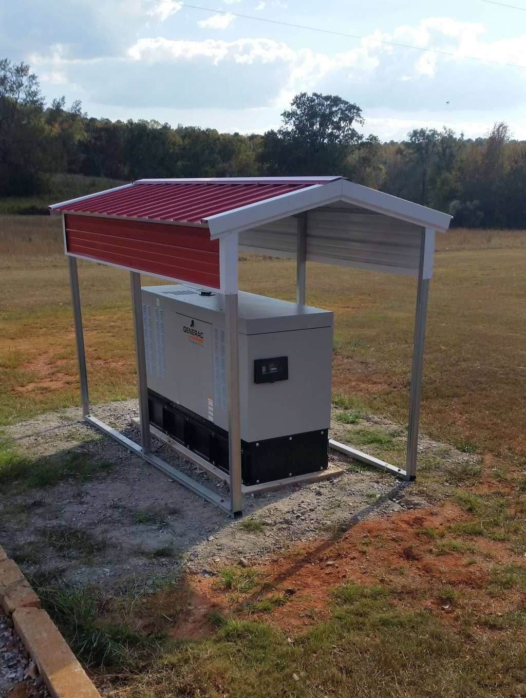 A generator is sitting under a red roof in a field.