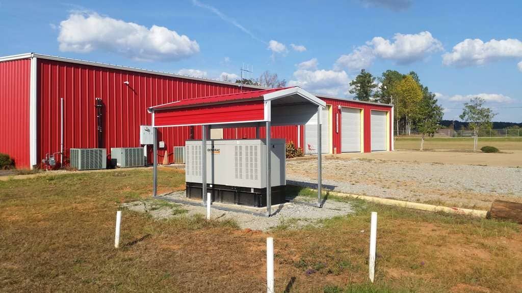 A red building with a white roof is sitting in the middle of a grassy field.