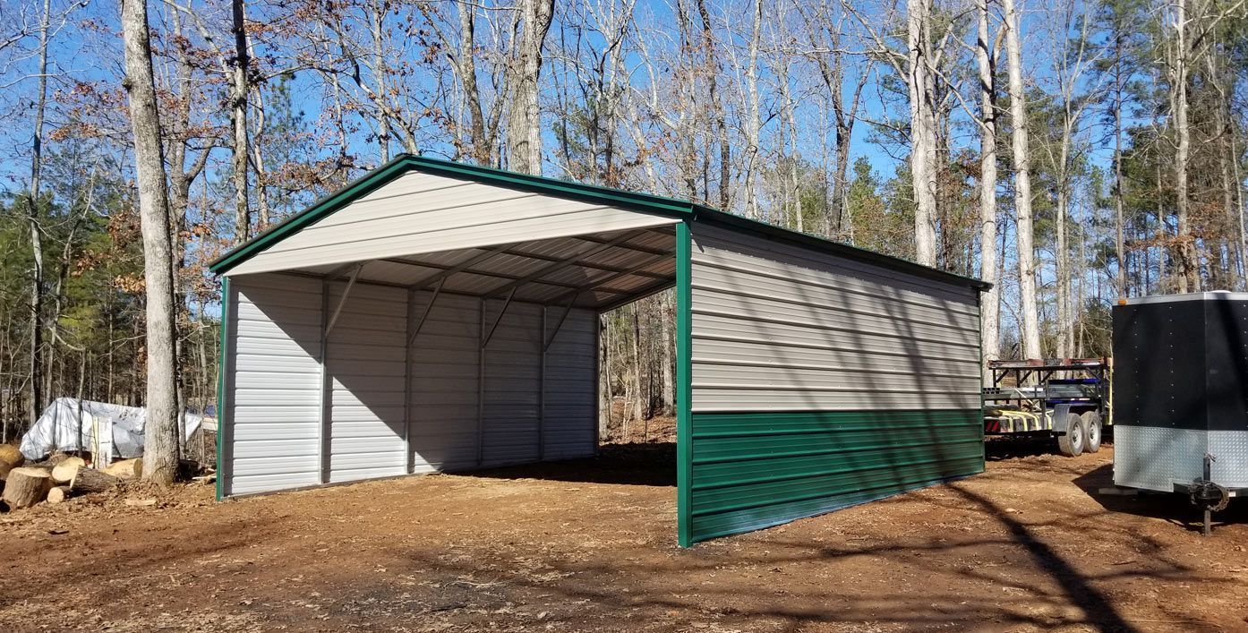 A white and green metal barn is sitting in the middle of a dirt field.