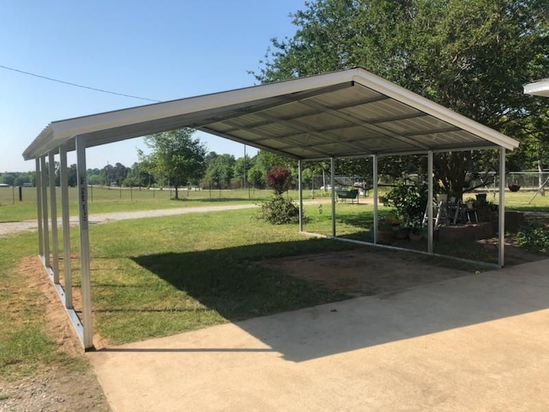 A carport is sitting in the middle of a driveway next to a grassy field.