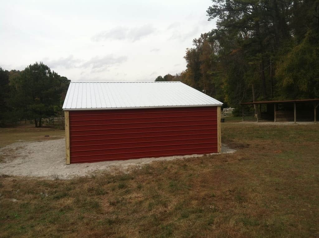 A red barn with a white roof is in the middle of a grassy field.