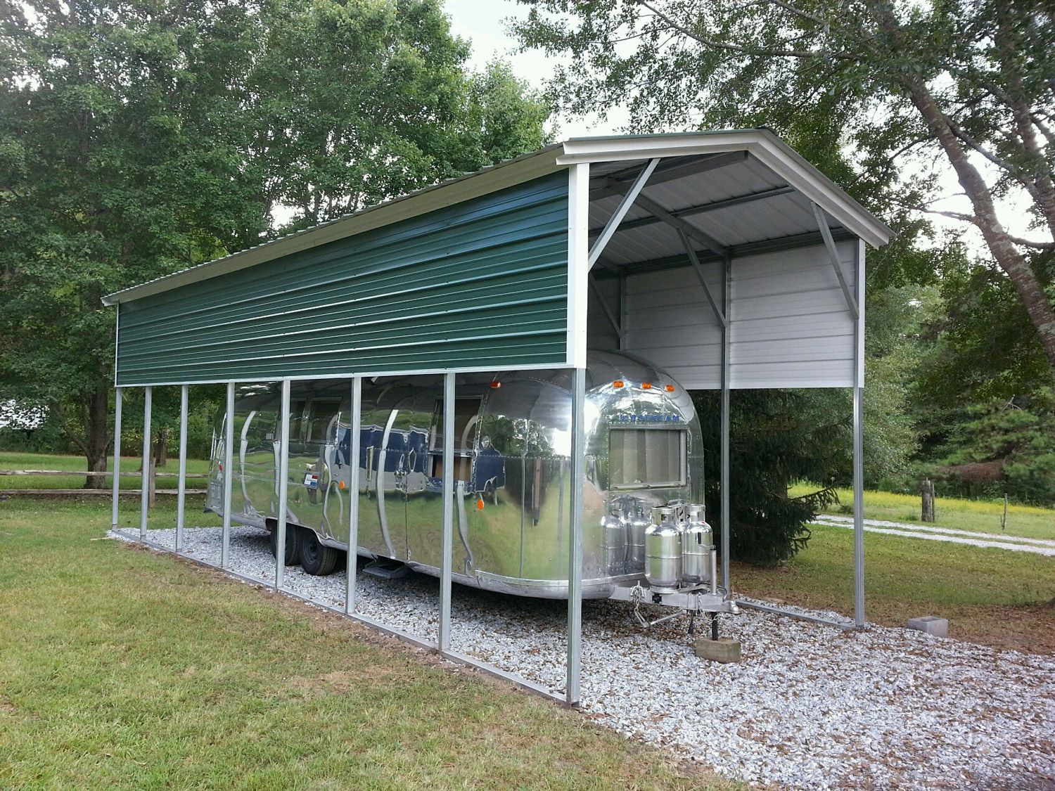 An airstream trailer is parked under a carport