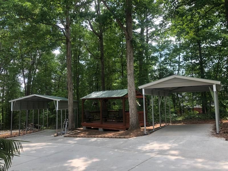 A row of carports in a driveway surrounded by trees.