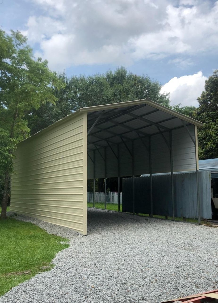 A metal carport is sitting on top of a gravel driveway.