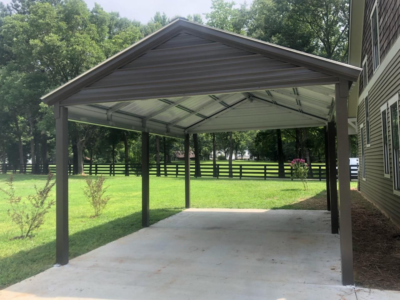 A carport is sitting in front of a house with a fence in the background.