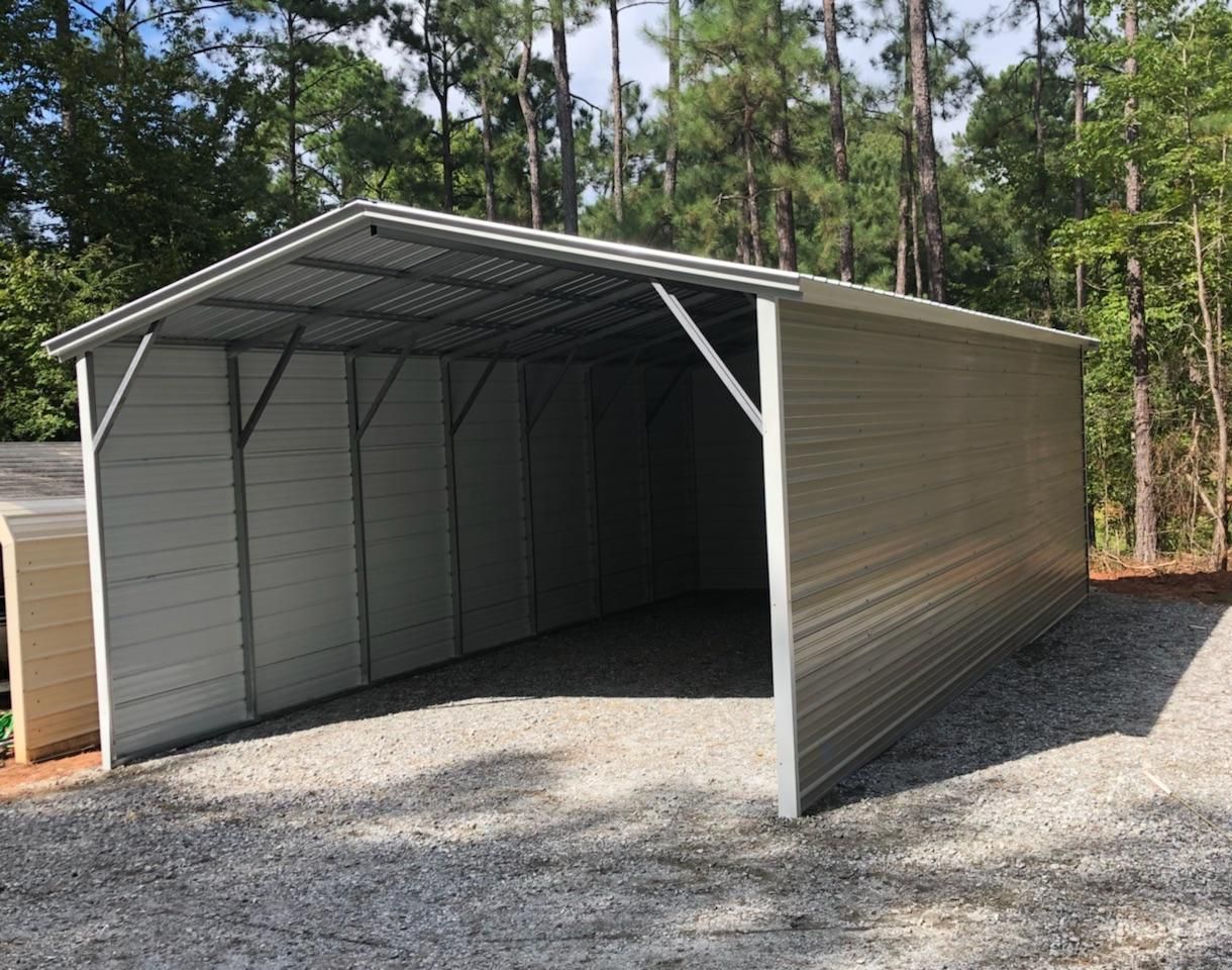A large white metal garage is sitting on top of a gravel driveway.