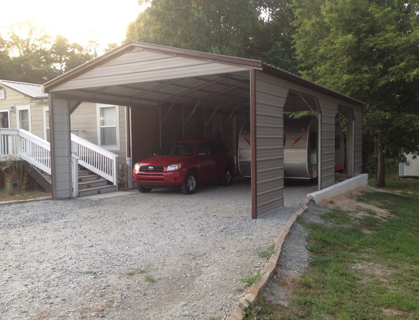 A red car is parked under a carport in front of a house.