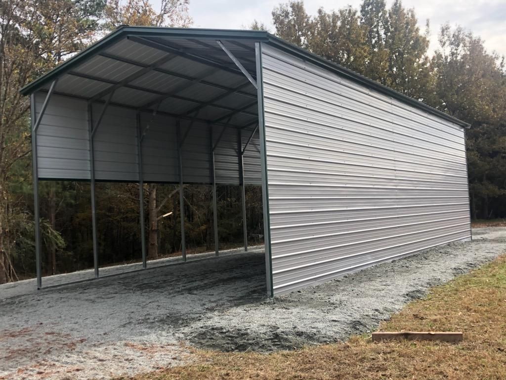 A metal carport is sitting on the side of a dirt road.