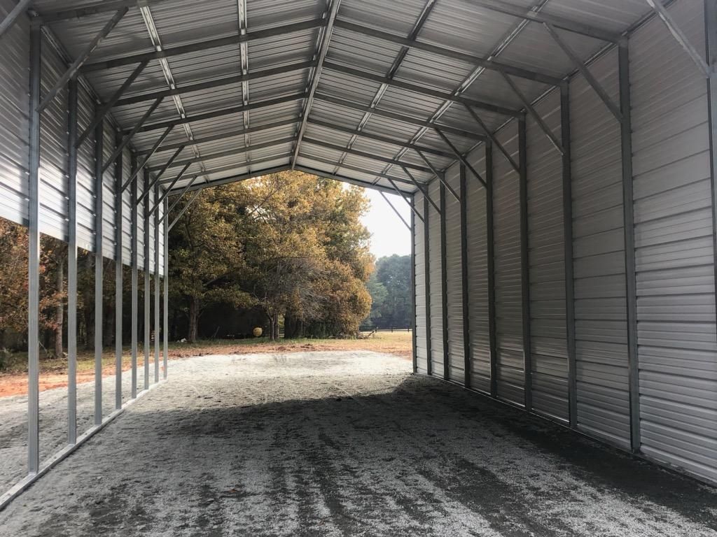 The inside of a metal carport with a gravel driveway and trees in the background.