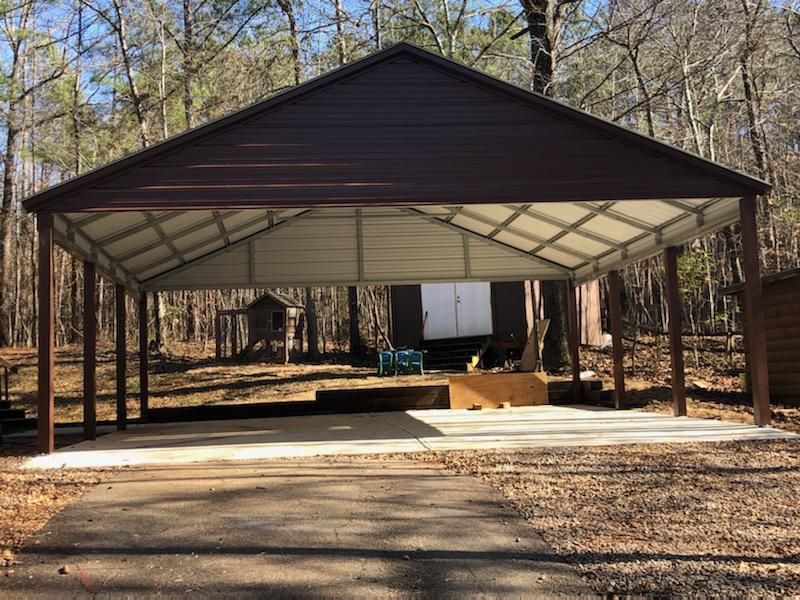 A large metal carport is sitting in the middle of a forest.