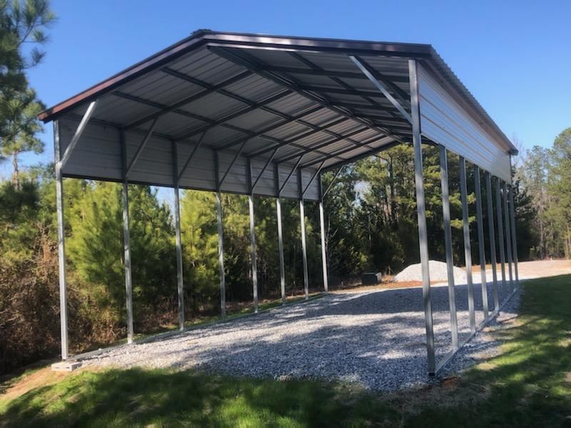A metal carport is sitting on top of a gravel driveway.