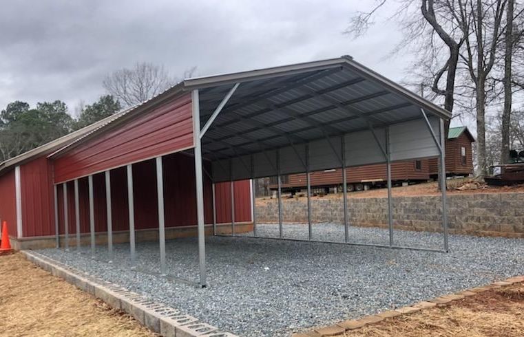 A red barn with a metal carport in front of it.