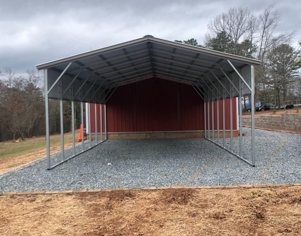 A red barn with a metal roof is sitting on top of a gravel lot.