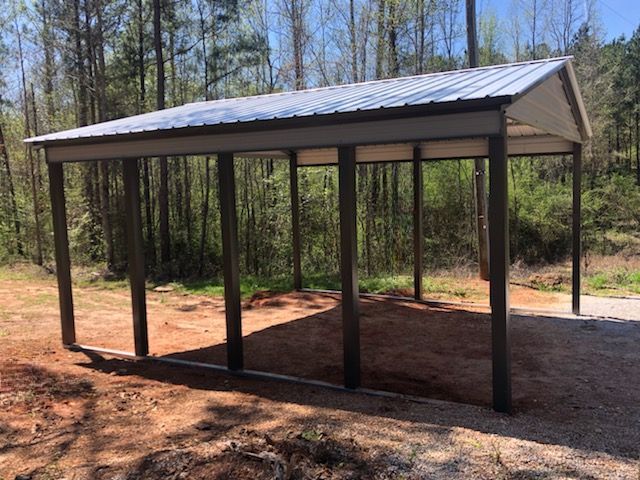 A metal carport is sitting in the middle of a dirt field.