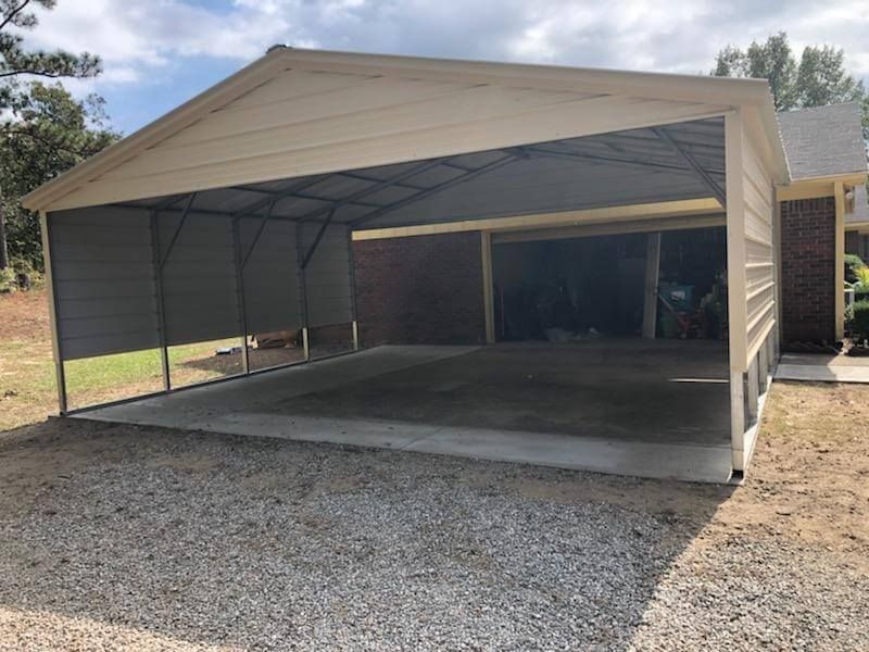 A carport is sitting on top of a gravel driveway in front of a house.
