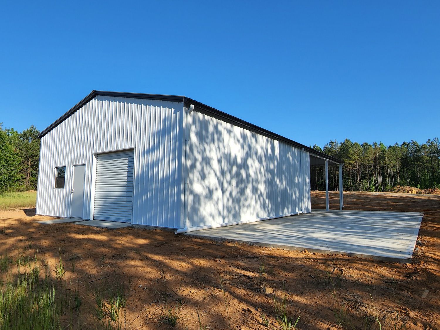 A white building with a black roof is sitting in the middle of a dirt field.