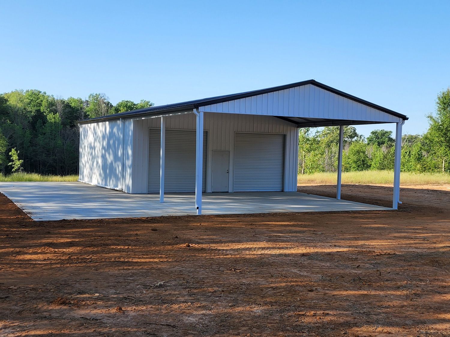A white garage with a canopy over it is sitting in the middle of a dirt field.