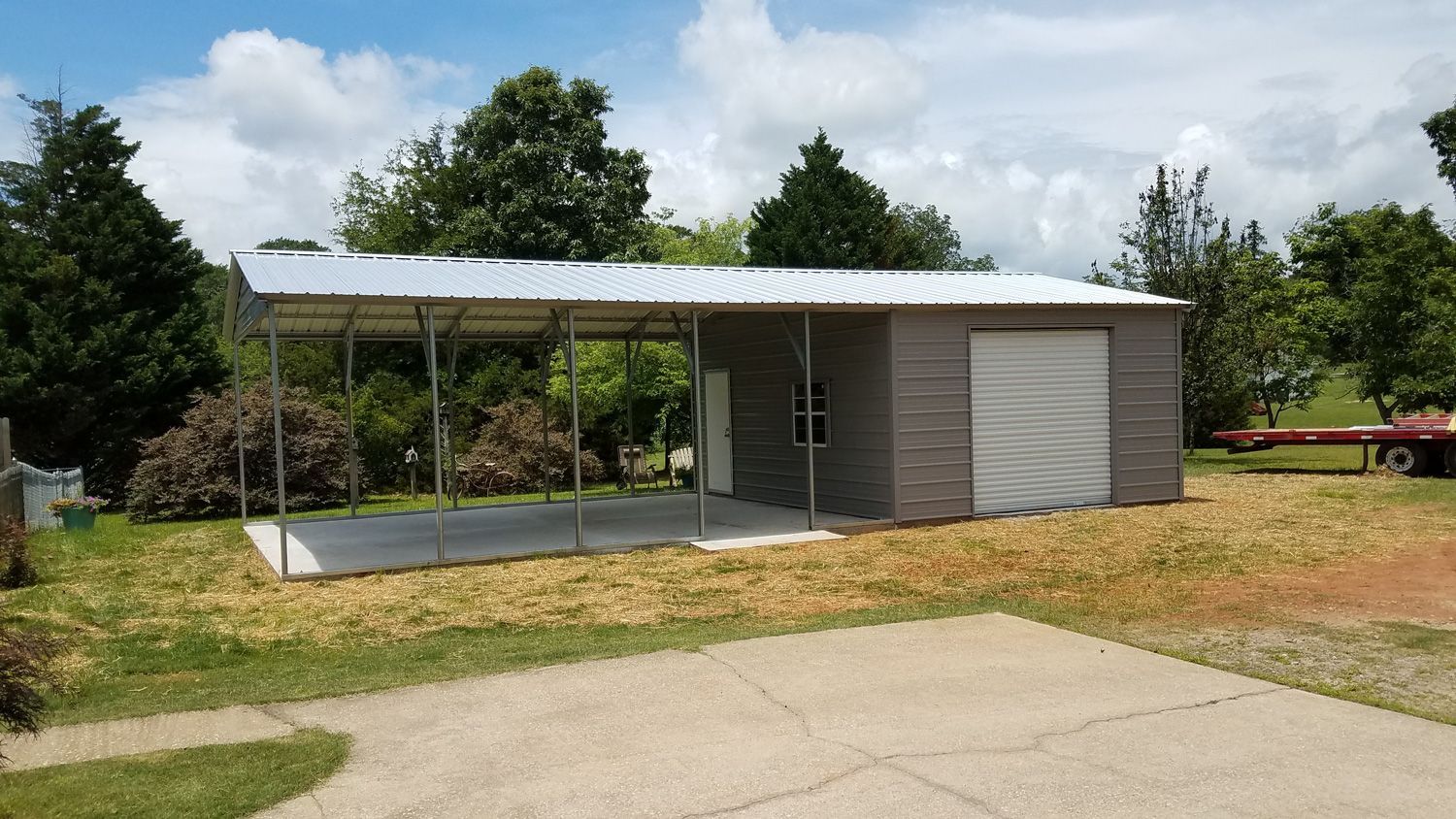 A metal garage with a white door is sitting in the middle of a grassy field.